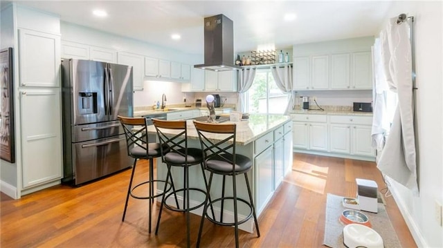 kitchen featuring stainless steel fridge, sink, island range hood, white cabinetry, and light wood-type flooring