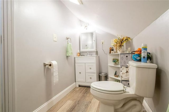 bathroom featuring wood-type flooring, lofted ceiling, vanity, and toilet