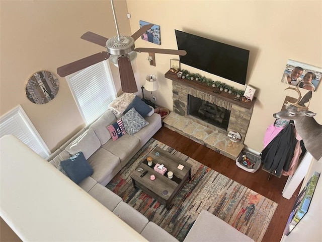living room with a stone fireplace, a ceiling fan, and wood finished floors