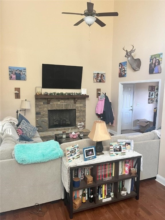 living room with ceiling fan, a stone fireplace, and dark wood-type flooring