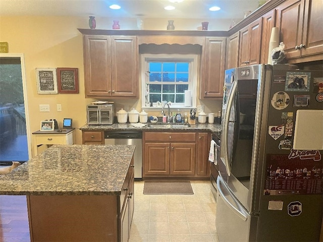 kitchen featuring stainless steel appliances, dark stone countertops, a center island, and sink