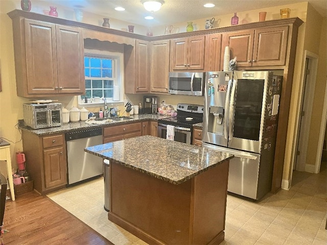 kitchen featuring appliances with stainless steel finishes, dark stone countertops, a center island, light hardwood / wood-style flooring, and sink