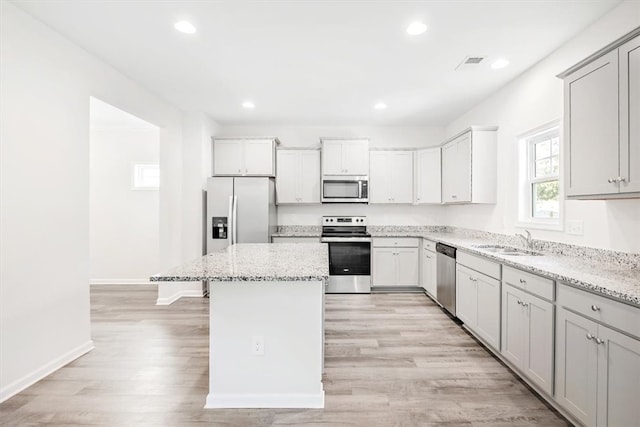 kitchen featuring a kitchen island, sink, stainless steel appliances, and light stone counters