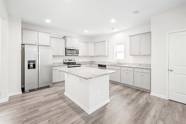 kitchen featuring light stone counters, stainless steel appliances, light wood-type flooring, and a center island