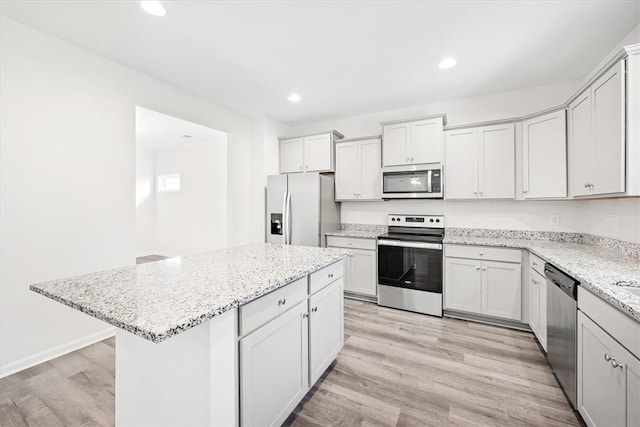 kitchen featuring light stone counters, white cabinets, stainless steel appliances, light wood-type flooring, and a center island