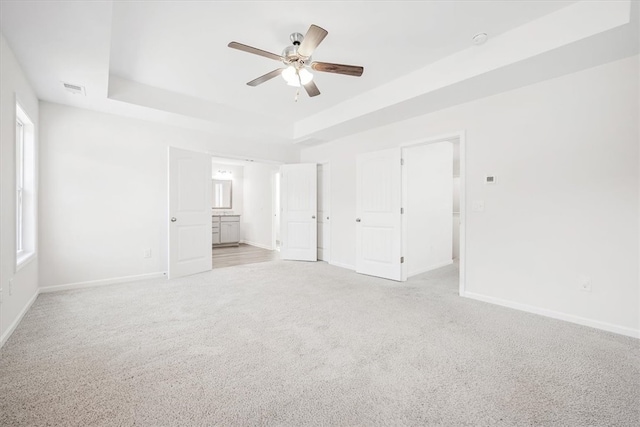 unfurnished bedroom featuring connected bathroom, a tray ceiling, light carpet, and ceiling fan