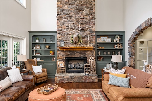 living room with a stone fireplace, hardwood / wood-style flooring, plenty of natural light, and a high ceiling