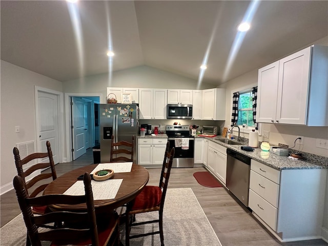 kitchen with light wood-type flooring, sink, white cabinets, vaulted ceiling, and appliances with stainless steel finishes