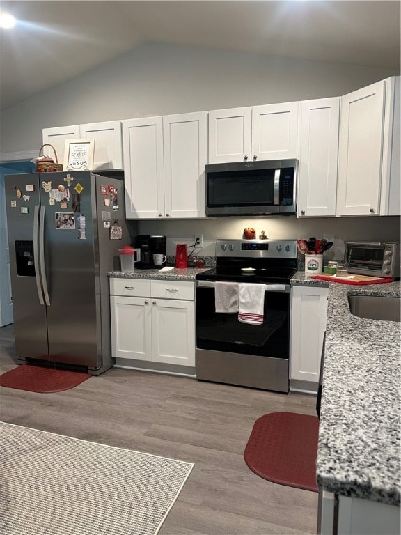 kitchen featuring light hardwood / wood-style floors, lofted ceiling, white cabinetry, stainless steel appliances, and light stone countertops