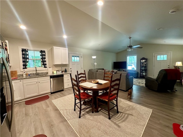 dining area with ceiling fan, vaulted ceiling, sink, and light hardwood / wood-style floors