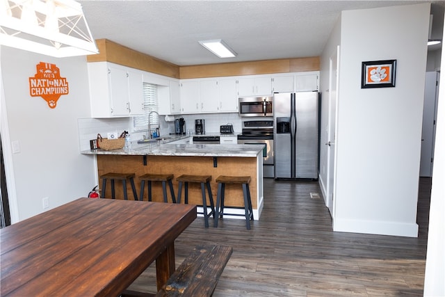 kitchen with kitchen peninsula, a textured ceiling, white cabinetry, appliances with stainless steel finishes, and dark hardwood / wood-style flooring