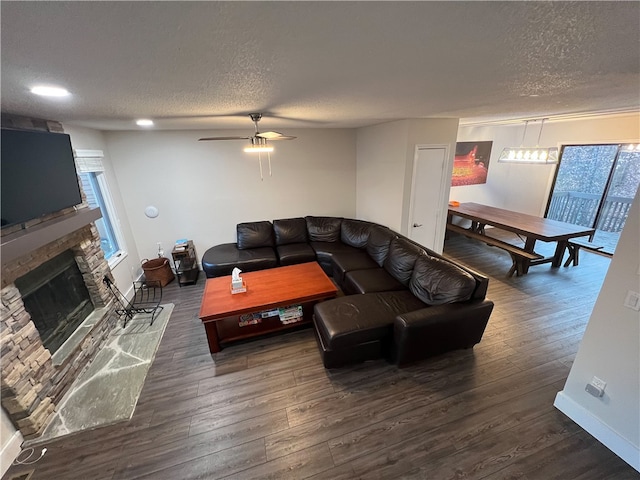 living room featuring ceiling fan, a stone fireplace, a textured ceiling, and dark hardwood / wood-style floors