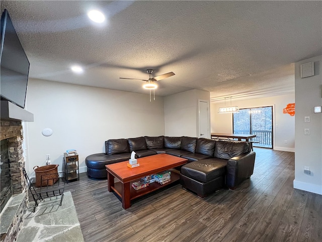 living room featuring a textured ceiling, dark hardwood / wood-style floors, ceiling fan, and a stone fireplace