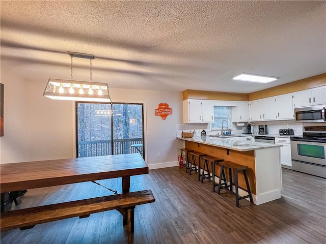 kitchen with light stone counters, pendant lighting, white cabinets, dark wood-type flooring, and stainless steel appliances