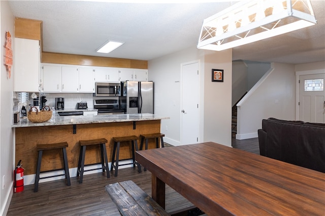 kitchen featuring appliances with stainless steel finishes, white cabinetry, tasteful backsplash, light stone countertops, and dark hardwood / wood-style floors