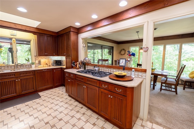 kitchen with sink, tasteful backsplash, stainless steel gas cooktop, decorative light fixtures, and light carpet