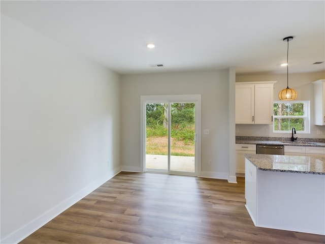 kitchen with light stone counters, white cabinets, pendant lighting, stainless steel dishwasher, and hardwood / wood-style floors