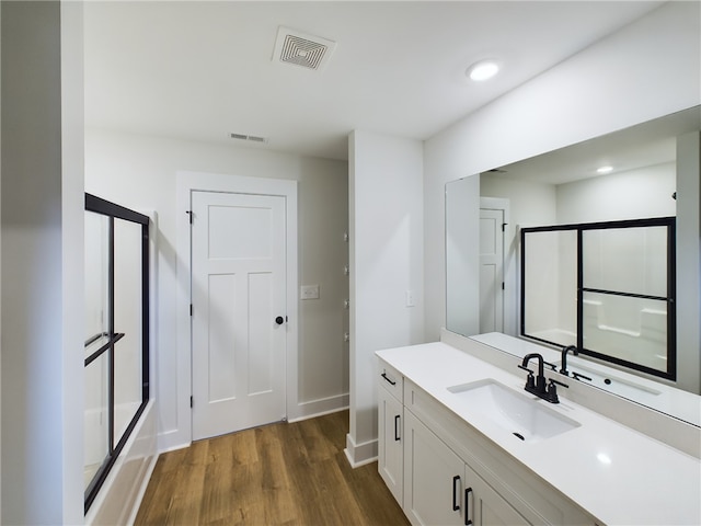 bathroom featuring wood-type flooring, vanity, and enclosed tub / shower combo