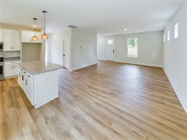 kitchen with light wood-type flooring, light stone countertops, white cabinetry, and a center island