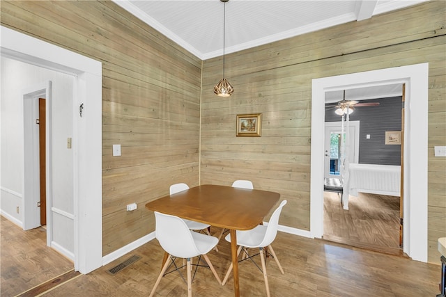 dining space featuring wood-type flooring, wood walls, and ceiling fan