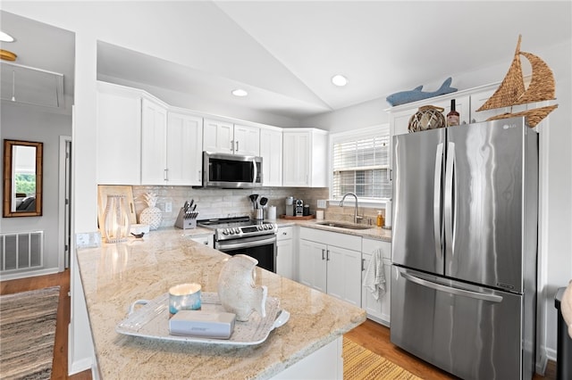 kitchen featuring vaulted ceiling, sink, light stone countertops, appliances with stainless steel finishes, and white cabinets