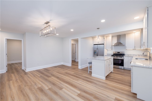 kitchen with a kitchen island, stainless steel appliances, decorative light fixtures, sink, and wall chimney range hood