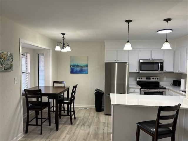 kitchen featuring a chandelier, hanging light fixtures, stainless steel appliances, white cabinets, and light hardwood / wood-style flooring