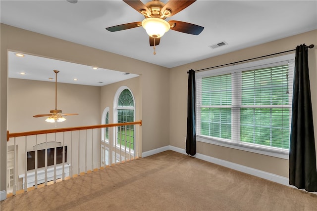 empty room featuring ceiling fan, light colored carpet, and a healthy amount of sunlight