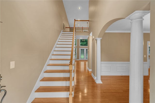 staircase featuring wood-type flooring, decorative columns, a high ceiling, and crown molding