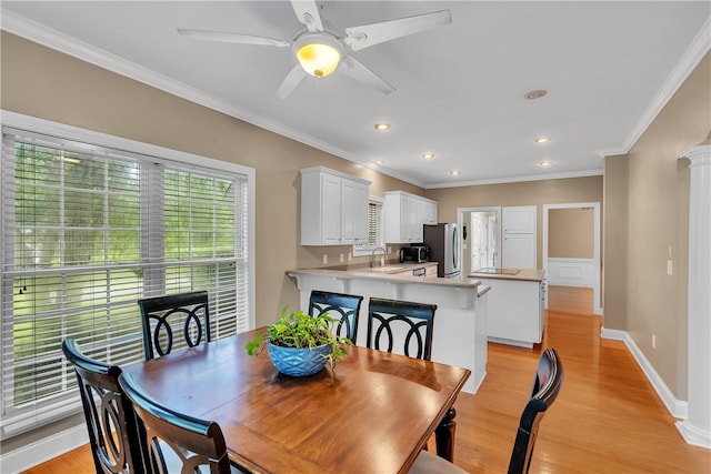 dining area with light wood-type flooring, sink, crown molding, ceiling fan, and ornate columns