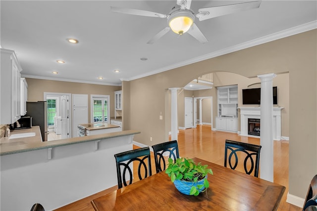 dining space with ceiling fan, sink, ornamental molding, light hardwood / wood-style flooring, and ornate columns