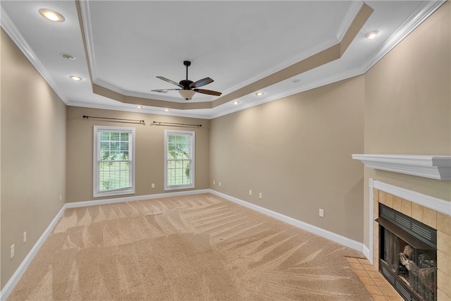 unfurnished living room with ornamental molding, a tray ceiling, light colored carpet, and a fireplace