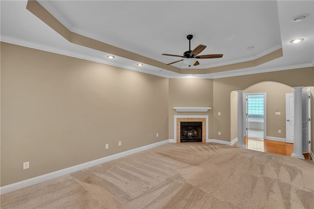 unfurnished living room with a tile fireplace, crown molding, a tray ceiling, and light carpet