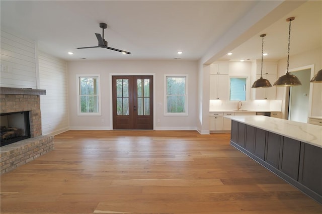 unfurnished living room with french doors, sink, light wood-type flooring, ceiling fan, and a fireplace