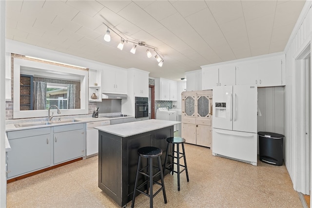 kitchen with black appliances, washing machine and dryer, white cabinetry, and a center island