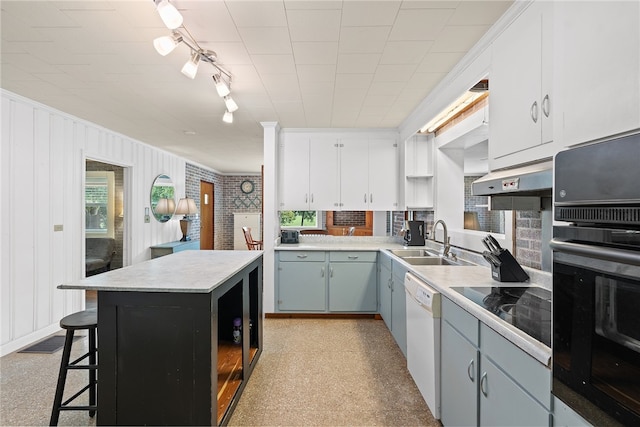 kitchen featuring dishwasher, sink, white cabinets, a kitchen bar, and stainless steel oven