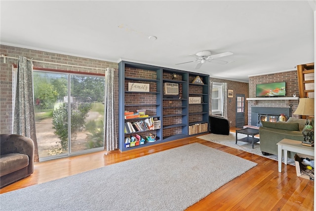 living area with ceiling fan, brick wall, hardwood / wood-style flooring, and a fireplace