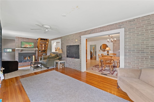 living room with a brick fireplace, wood-type flooring, ceiling fan, and crown molding