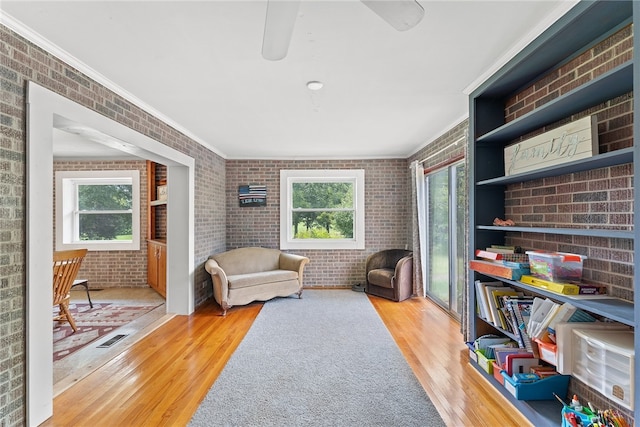 sitting room with brick wall, hardwood / wood-style flooring, a healthy amount of sunlight, and crown molding