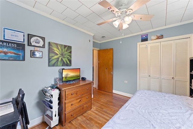 bedroom with ceiling fan, a closet, ornamental molding, and wood-type flooring