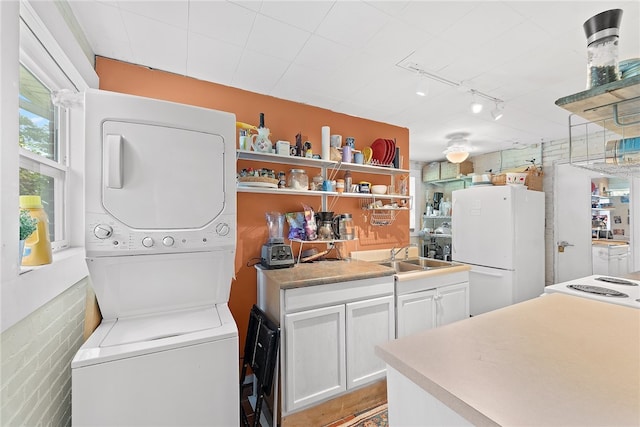 laundry room with track lighting, stacked washer / dryer, and sink