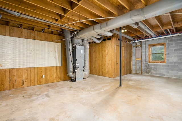 basement featuring wood walls and heating unit