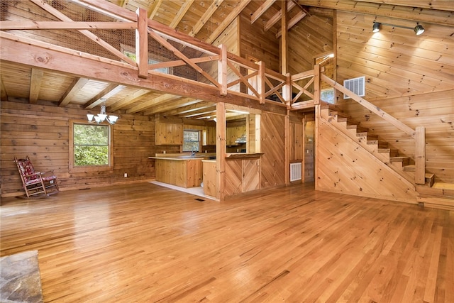 unfurnished living room with lofted ceiling with beams, light wood-type flooring, wooden ceiling, an inviting chandelier, and wooden walls