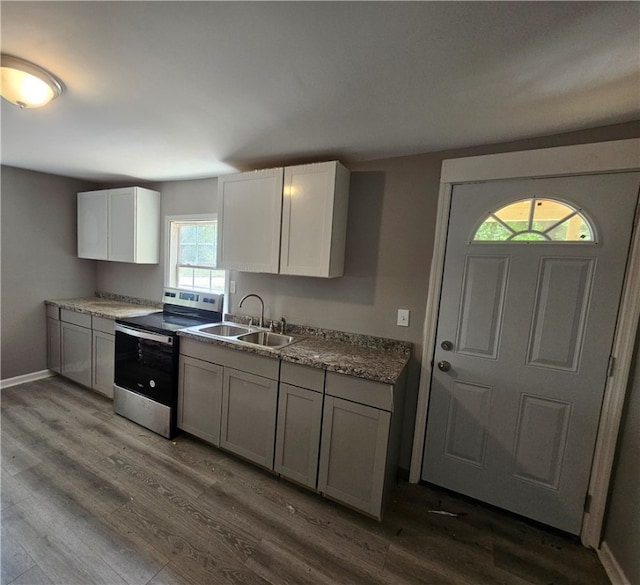 kitchen featuring white cabinetry, stainless steel electric range, light stone counters, wood-type flooring, and sink