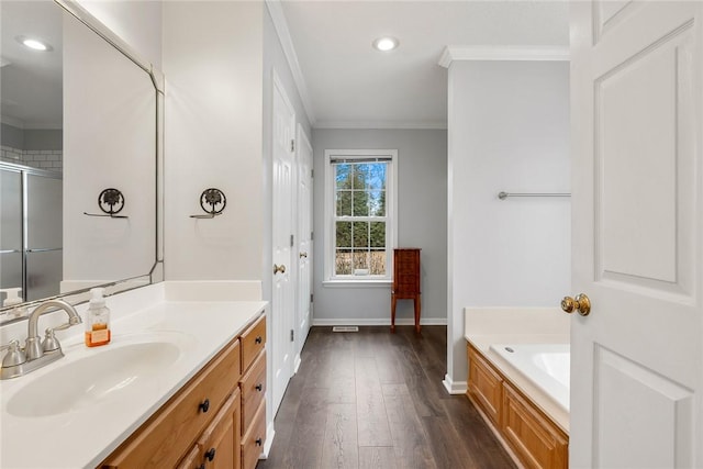 bathroom with crown molding, vanity, wood finished floors, baseboards, and a bath