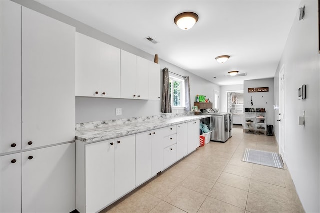 kitchen with white cabinets, washer / dryer, light stone counters, and light tile patterned floors