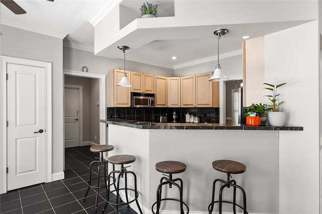 kitchen featuring kitchen peninsula, light brown cabinetry, appliances with stainless steel finishes, decorative light fixtures, and decorative backsplash