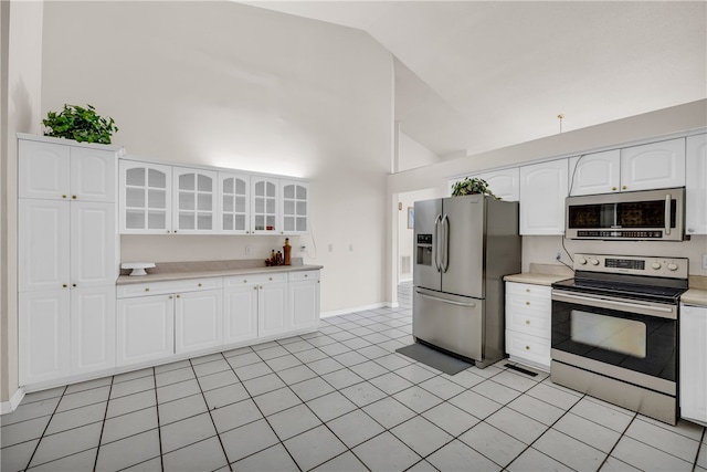 kitchen with appliances with stainless steel finishes, white cabinetry, light tile patterned floors, and high vaulted ceiling