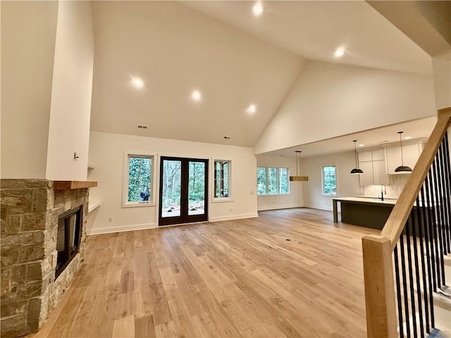 unfurnished living room featuring stairway, high vaulted ceiling, light wood-style flooring, a fireplace, and french doors