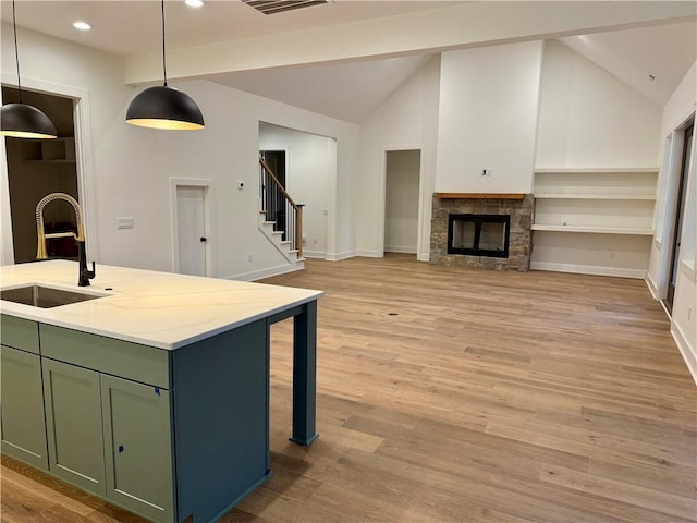 kitchen with open floor plan, green cabinetry, vaulted ceiling, light wood-style flooring, and a sink